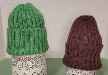 two hats are placed over lacy forms sitting on a green tablecloth. The hat on the left is green, and the one on the right a chocolate brown.